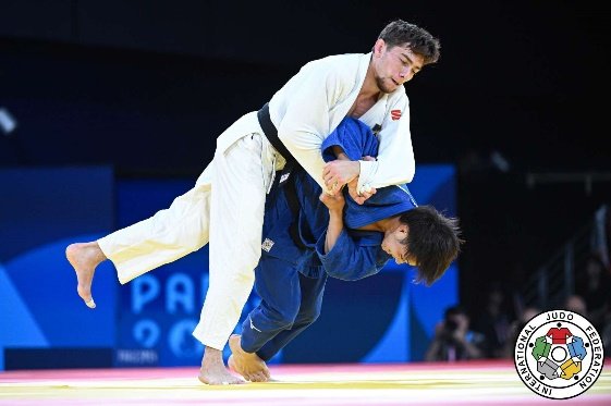 El judoka Hifumi Abe con judogi azul ejecutando un desequilibrio dinámico por debajo de la línea de defensa de su rival con judogi blanco en París 2024