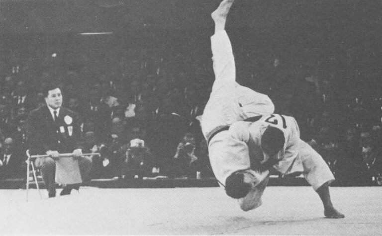 Fotografía histórica en blanco y negro del judoka Isao Inokuma ejecutando una proyección de gran elevación en una competencia oficial.