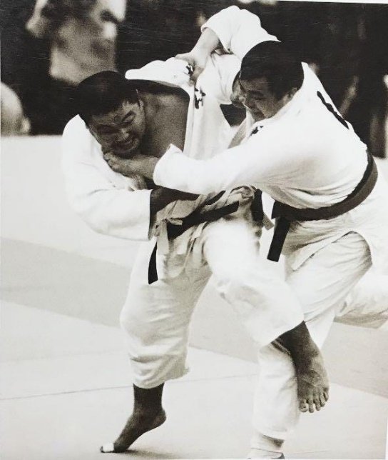 Fotografía histórica en blanco y negro del judoka Yasuhiro Yamashita disputando un agarre e iniciando una técnica de pierna en el tatami.