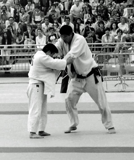 Fotografía histórica en blanco y negro del judoka Haruki Uemura controlando el agarre durante un combate en un torneo al aire libre.