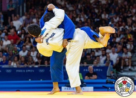 El judoka Takanori Nagase, con el dorsal oficial de los Juegos Olímpicos de París 2024, disputando una proyección aérea frente a un rival con judogi azul.
