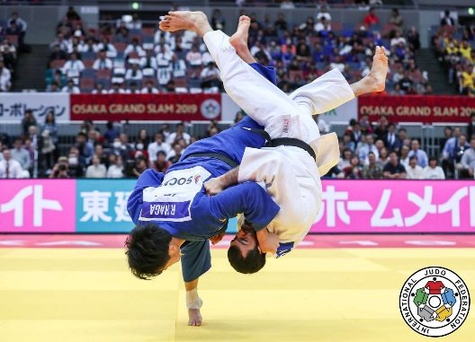 El judoka Ryunosuke Haga con judogi azul ejecutando una proyección aérea alta (Uchi-mata) contra un oponente con judogi blanco durante el Grand Slam de Osaka 2019.