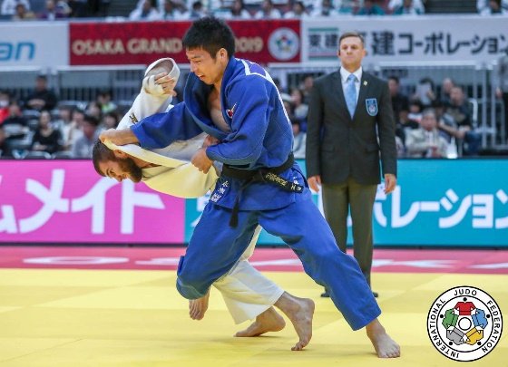 El judoka Takanori Nagase con judogi azul controlando el agarre de solapa y manga frente a Anri Egutidze en el Grand Slam de Osaka 2019