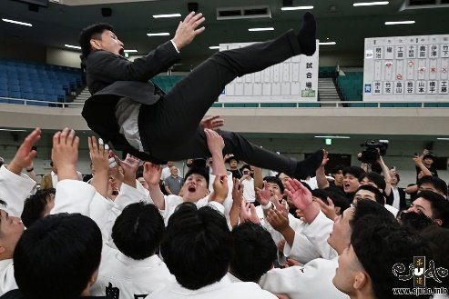 Los competidores de judo de la Universidad de Meiji con judogi blanco lanzando al aire a su director técnico en traje formal para celebrar la victoria.