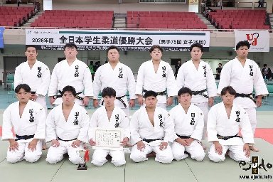 El equipo masculino de judo de la Universidad Kokushikan posando de rodillas y de pie con un diploma oficial sobre el tatami del Nippon Budokan.