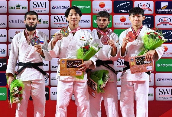 El judoka japonés Takeshi Takeoka en el centro del podio sosteniendo su medalla de oro y un ramo de flores junto a los demás medallistas internacionales.