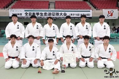 El equipo masculino de judo de la Universidad de Tokai posando alineado con diplomas oficiales y un trofeo pequeño sobre el tatami del Nippon Budokan.