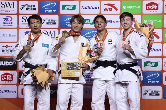 El judoka japonés Hifumi Abe en el centro del podio sosteniendo su medalla de oro y un ramo de flores junto a los medallistas de Kazajistán, Brasil y Francia.