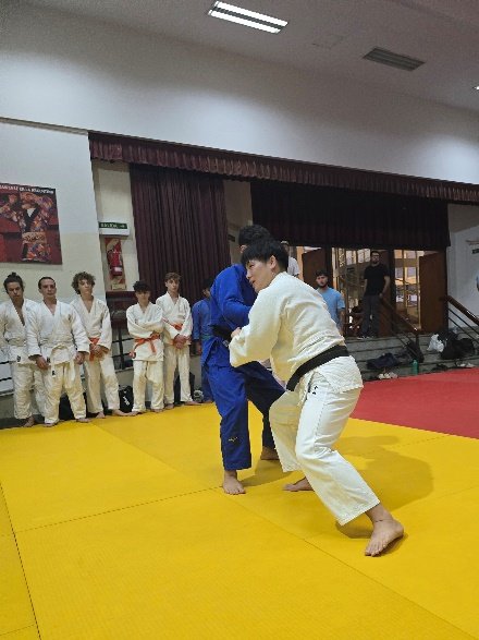 Un judoka con judogi blanco flexiona las piernas e inicia el desequilibrio de agarre frente a su compañero con judogi azul durante un combate de práctica.