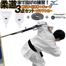 Un judoka con judogi blanco ejecutando una entrada de proyección en casa utilizando un kit Mizuno con banda de goma y anclaje sujeto a una puerta.