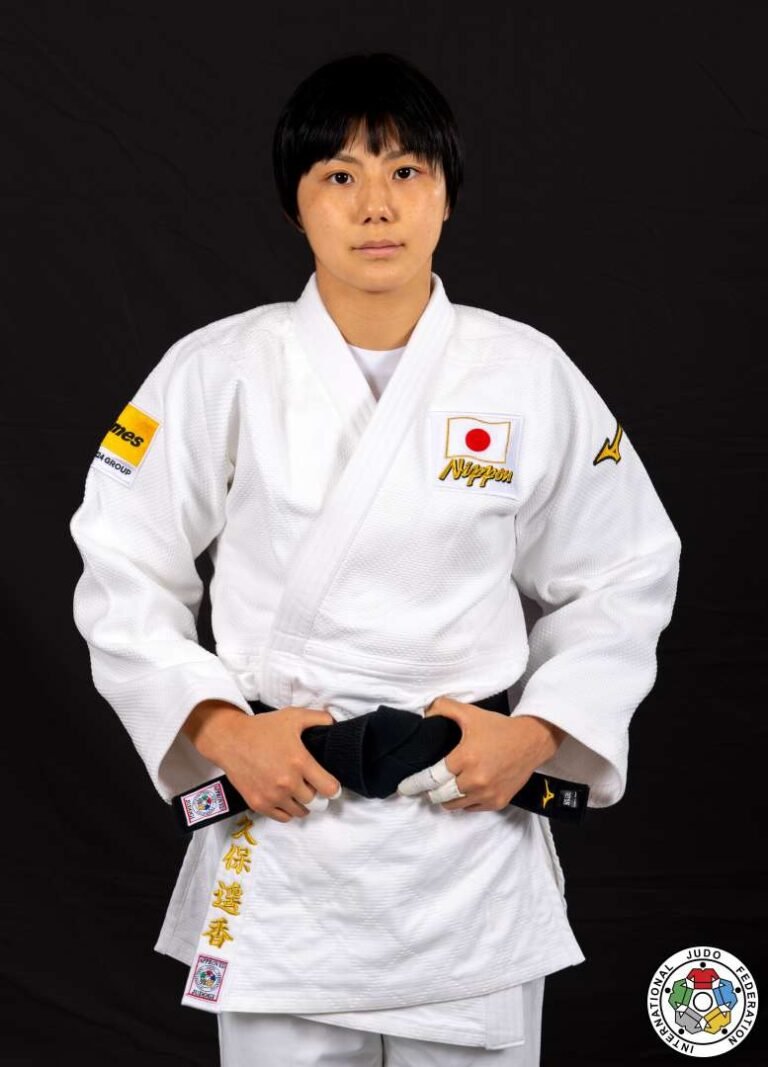 Retrato de estudio en plano medio de una judoka japonesa vistiendo judogi blanco con la bandera de Japón, cinturón negro y el sello oficial de la IJF.