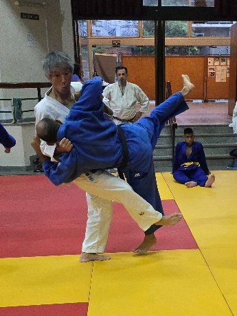 El maestro de judo Seishi Yanagida ejecutando una proyección sobre un judoka con judogi azul durante una práctica técnica en el dojo.