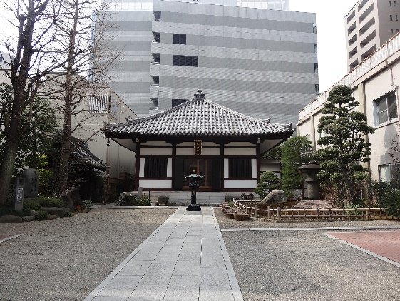 Vista frontal del templo tradicional Eisho-ji en Tokio con un patio de grava y senderos de piedra, rodeado por edificios modernos.